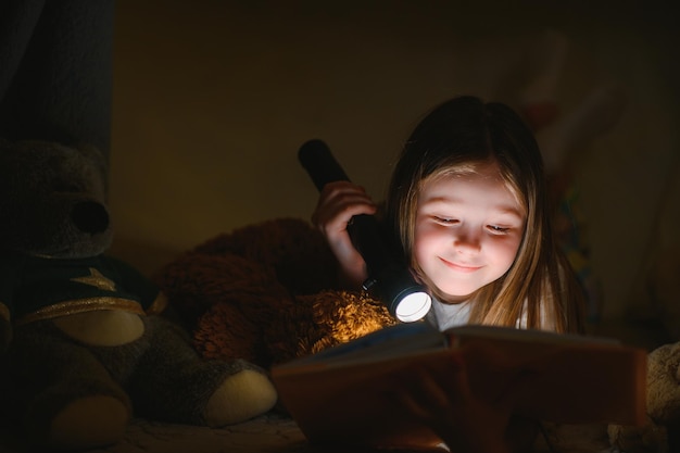 Niña está leyendo un libro con linternas en la tienda Niña feliz jugando en casa Niño encantador divertido divirtiéndose en la habitación