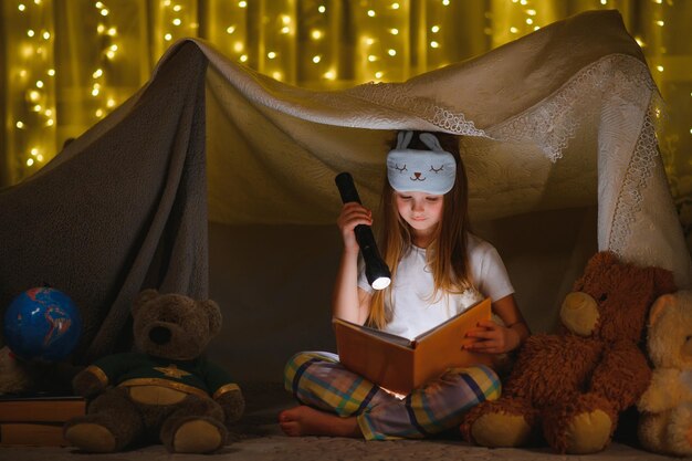 Niña está leyendo un libro con linternas en la tienda Niña feliz jugando en casa Niño encantador divertido divirtiéndose en la habitación