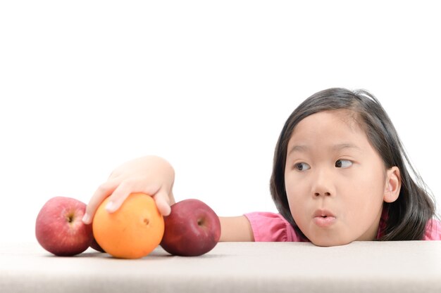 niña está llegando a naranja en la mesa aislada