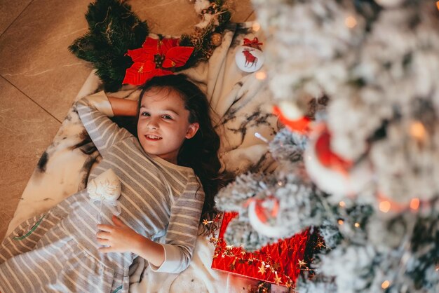 la niña está mintiendo y riendo bajo el árbol de navidad