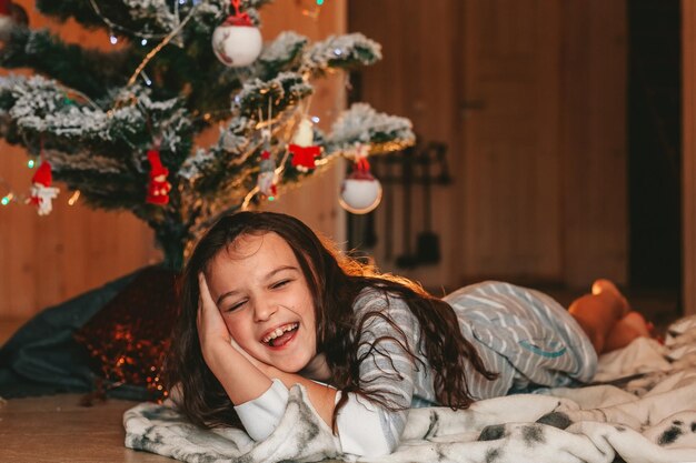 la niña está mintiendo y riendo bajo el árbol de navidad