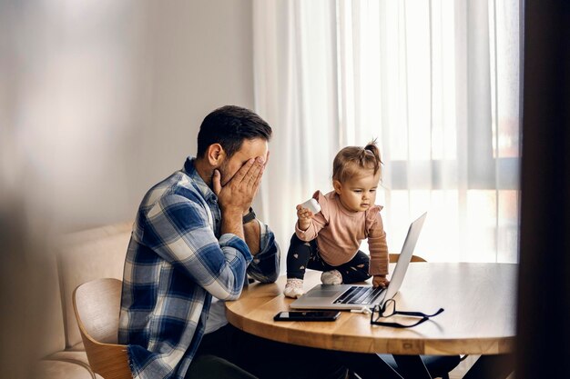 Una niña está molestando a su padre en su trabajo desde casa en una computadora portátil