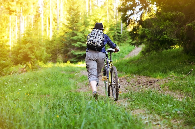 La niña está montando una bicicleta en el bosque en el verano en las montañas.