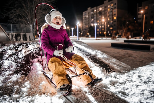 Una niña está paseando en trineo en una noche de invierno nevada