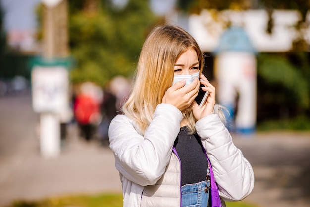 La niña está de pie junto a la carretera con una máscara médica protectora. Denso smog en las calles de la ciudad.