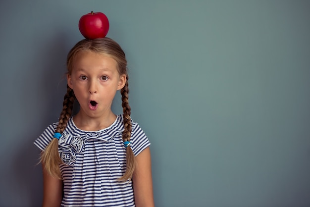 Niña está de pie con manzana roja en la cabeza