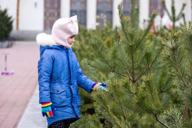 Una niña está de pie y mirando los copos de nieve que caen sobre el fondo de abetos de color verde oscuro.