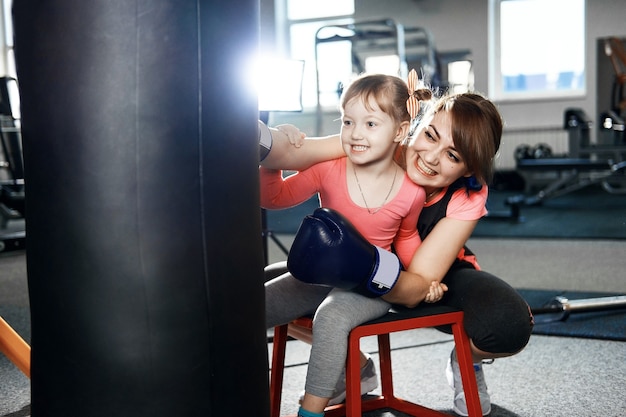 Niña está practicando boxeo, niña enseña a mamá a boxear, madre e hija divertidas en el gimnasio