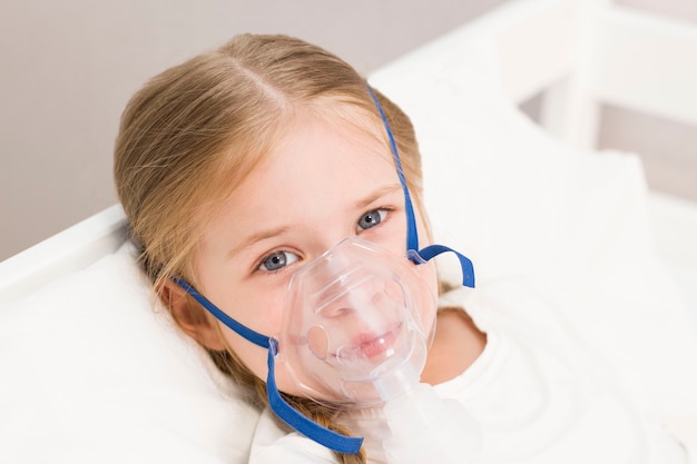 La niña está respirando a través de un inhalador. un niño enfermo está acostado en la cama