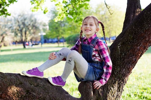 La niña está sentada en el árbol y sonriendo