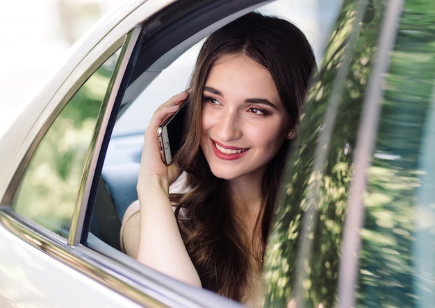 Una niña está sentada en el asiento trasero de un automóvil y está hablando por teléfono.