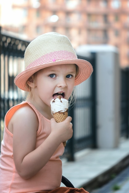 Una niña está sentada en el banco y comiendo helado. Un niño hermoso