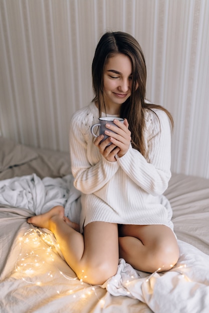 La niña está sentada en la cama con una taza.