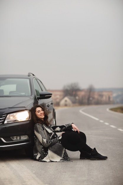 La niña está sentada en la carretera cerca de un auto negro