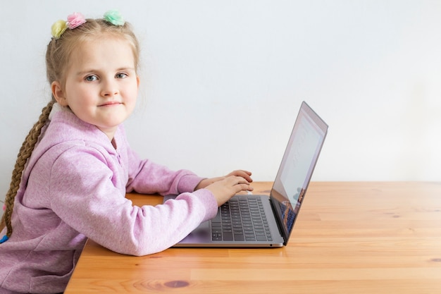 Una niña está sentada en una computadora portátil y está mirando a la cámara. Concepto de aprendizaje en línea