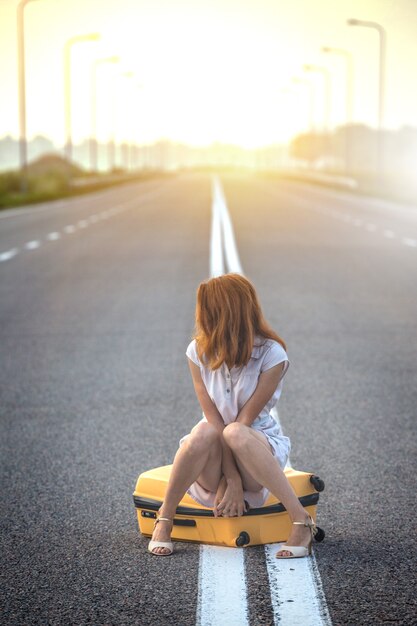 la niña está sentada en una maleta amarilla en la franja divisoria en la carretera