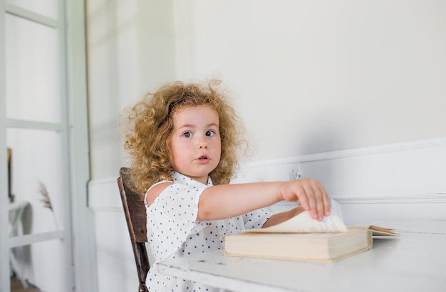 Una niña está sentada en una mesa frente a un libro abierto.