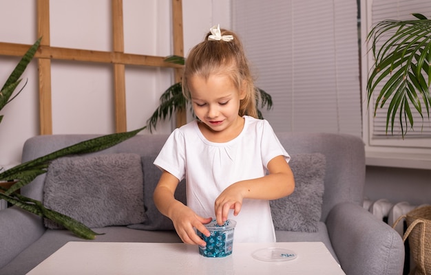 Una niña está sentada en una mesa y jugando con limo.