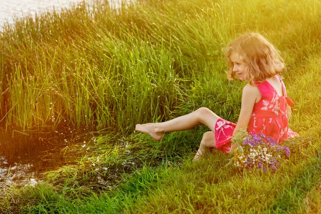 La niña está sentada en la orilla del lago