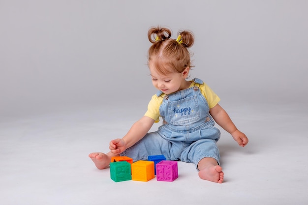 Una niña está sentada sobre un fondo blanco y jugando con cubos de colores cubos de juguete para niños