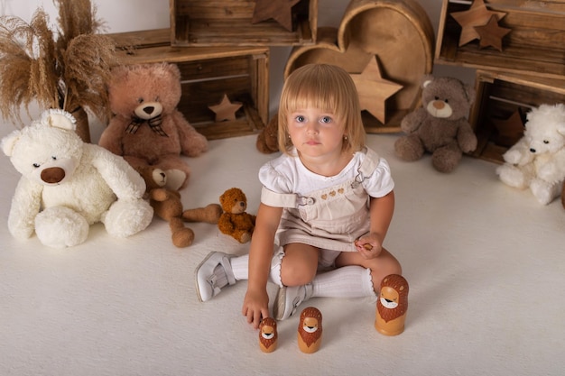 Una niña está sentada sobre un fondo blanco con osos de peluche y jugando con un juguete de cachorro de león.