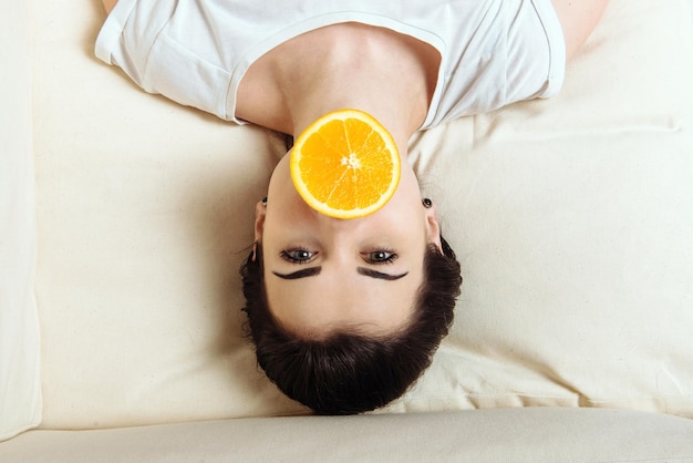 La niña está con un trozo de naranja en la boca.