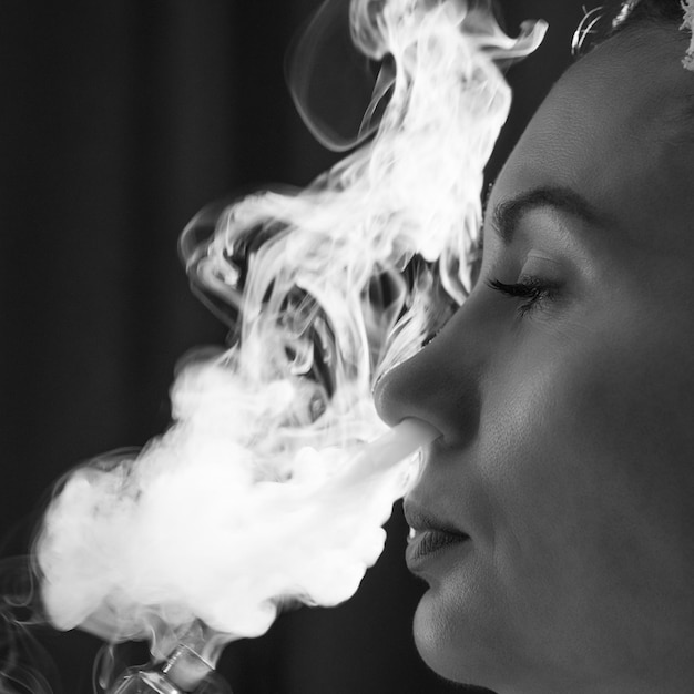 Una niña está vapeando un vaper libera humo de su boca cigarrillos electrónicos y un primer plano de niña