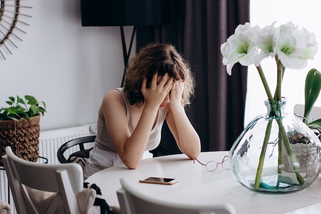 Niña en estado de shock sentada a la mesa en la sala de estar. Adolescente llorando