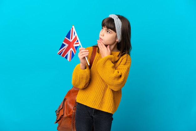 Niña estudiando inglés aislado en la pared azul mirando hacia arriba mientras sonríe