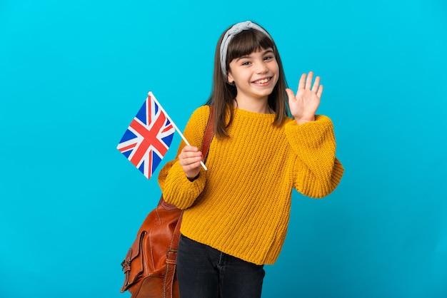 Niña estudiando inglés aislado en la pared azul saludando con la mano con expresión feliz