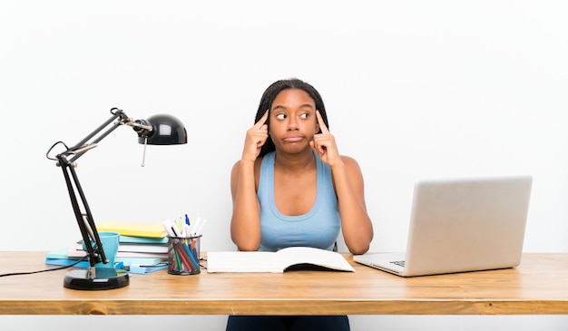 Niña estudiante afroamericana adolescente con cabello largo trenzado en su lugar de trabajo con dudas y pensamientos