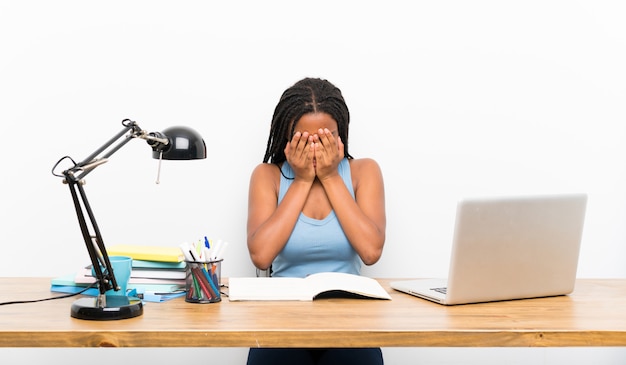 Niña estudiante afroamericana adolescente con cabello largo trenzado en su lugar de trabajo con expresión cansada y enferma