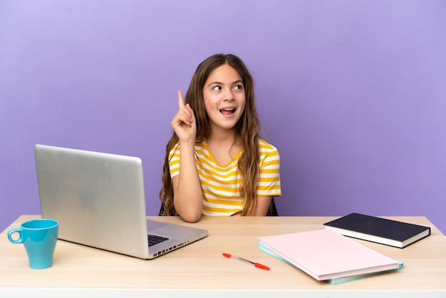 Niña estudiante en un lugar de trabajo con una computadora portátil aislada sobre fondo púrpura con la intención de darse cuenta de la solución mientras levanta un dedo hacia arriba