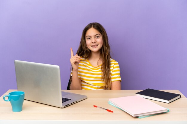 Niña estudiante en un lugar de trabajo con una computadora portátil aislada sobre fondo púrpura mostrando y levantando un dedo en señal de lo mejor