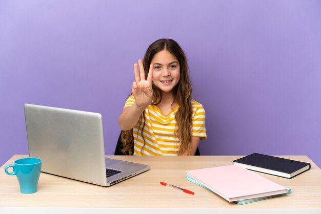 Niña estudiante en un lugar de trabajo con un portátil aislado sobre fondo púrpura feliz y contando tres con los dedos