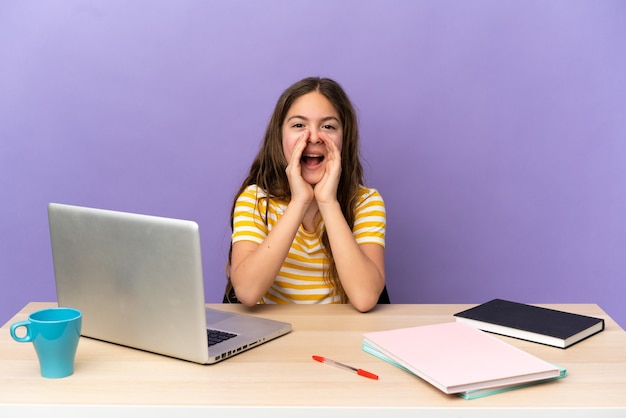 Niña estudiante en un lugar de trabajo con un portátil aislado sobre fondo púrpura gritando y anunciando algo