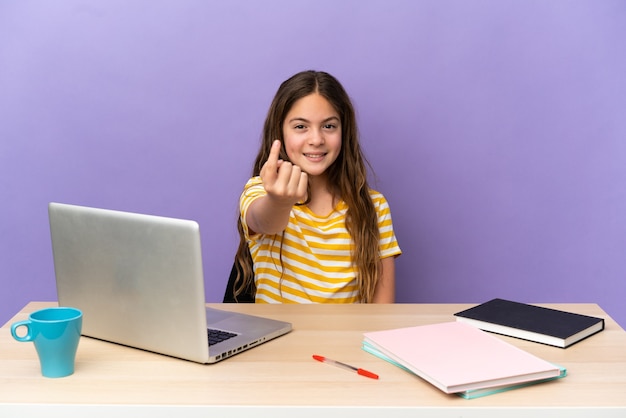 Niña estudiante en un lugar de trabajo con un portátil aislado sobre fondo púrpura haciendo gesto de venida