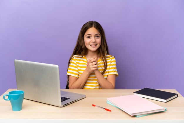 Niña estudiante en un lugar de trabajo con un portátil aislado sobre fondo púrpura riendo