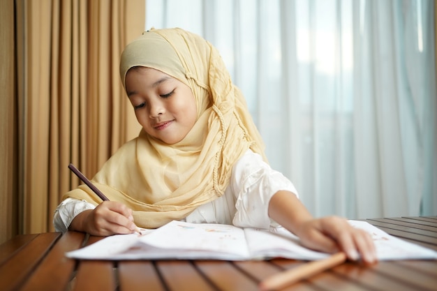 Niña estudiante musulmana escribiendo en el libro de papel.