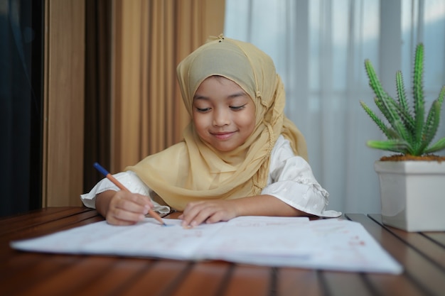 Niña estudiante musulmana escribiendo en el libro de papel