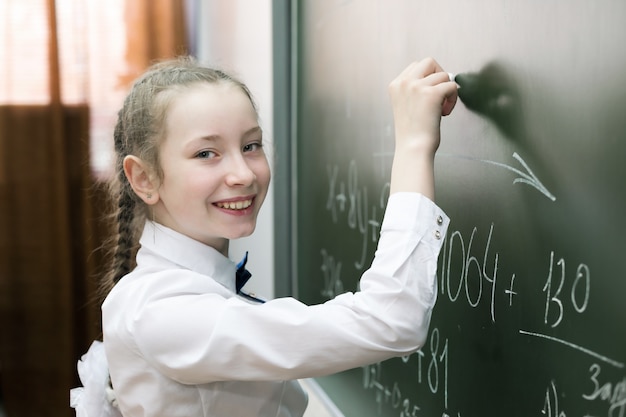 Una niña estudiante de primaria escribe en la pizarra.