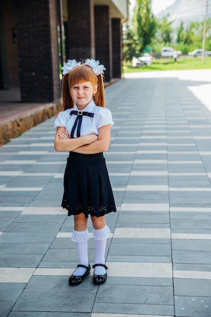 Una niña, estudiante de primaria, está parada en la calle con las manos cruzadas.