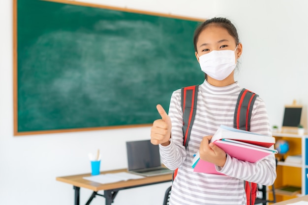 niña estudiante de primaria pulgar hacia arriba y con máscaras