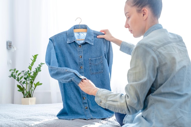 Una niña examinando ropa para vender en línea, sentada en la cama en casa. Reventa ir ropa.