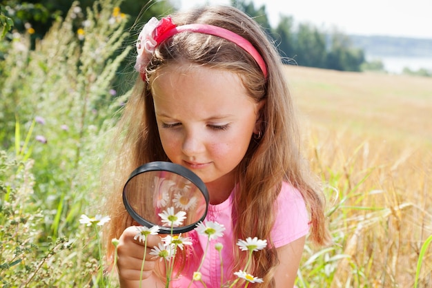 Niña explorando la flor de la margarita a través de la lupa al aire libre