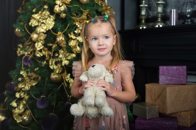 Niña feliz abraza a su juguete favorito en la habitación decorada para Navidad