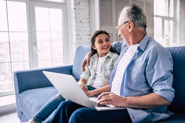 La niña feliz y un abuelo usando una computadora portátil en el sofá