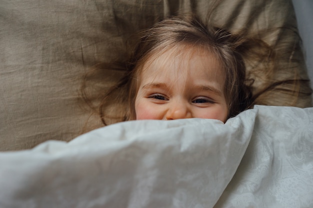 Foto niña feliz acostado en la cama, escondido debajo de la manta