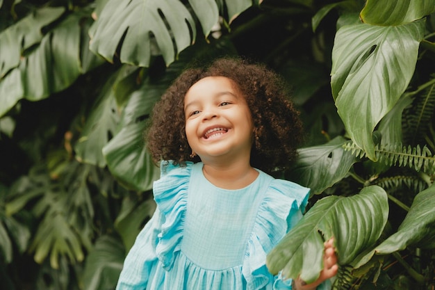 Niña feliz afroamericana en el fondo de hojas decorativas en el jardín