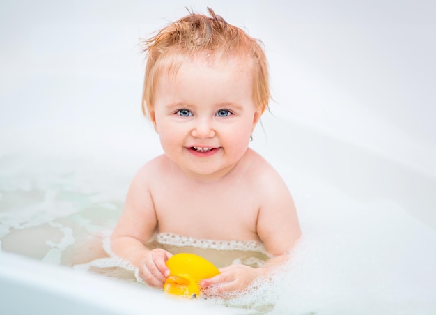 una niña feliz de un año se baña en un baño con un pato